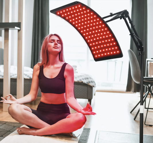 A person sitting in a meditation pose in front of a curved LED light therapy panel that is illuminated with red lights. It is an ideal LED device purchase.