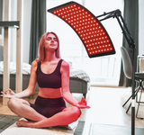 A person sitting in a meditation pose in front of a curved LED light therapy panel that is illuminated with red lights. It is an ideal LED device purchase.