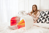 Woman using a white portable Esthelux device with colorful display on a bed. It is an ideal value LED device purchase.